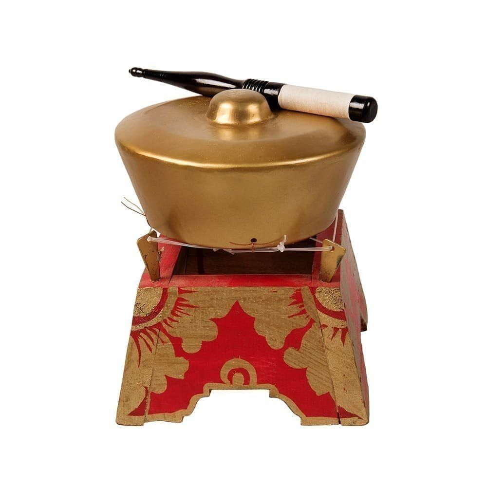 This is a product image of the Bonang - 1 Pan - Premium - Medium. It is a gold coloured pan with a gold boss on the top suspended by wire on a wooden frame. The frame is red with gold detail. There is a wooden beater that is wrapped in string at one end laying on the pan. The image has been taken from a head on position.