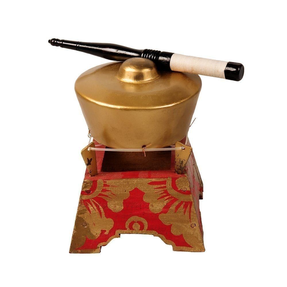 This is a product image of the Bonang - 1 Pan - Premium - Small. It is a gold coloured pan with a gold boss on the top suspended by wire on a wooden frame. The frame is red with gold detail. There is a wooden beater that is wrapped in string at one end laying on the pan. The image has been taken from a head on position.