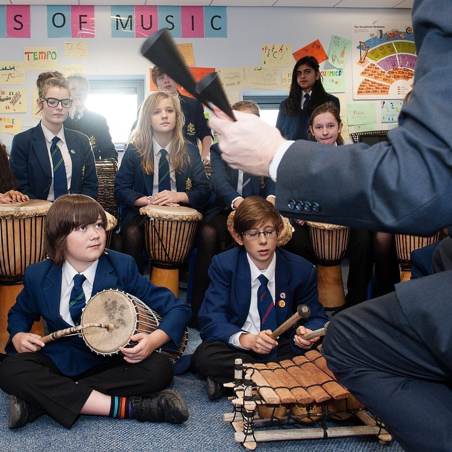 This is an action shot of some Secondary Schools children playing in a music workshop. They have a selection of West African instruments including a Talking Drum, a Balafon and Djembes. The teacher is partially in shot at the front with an Agogo.