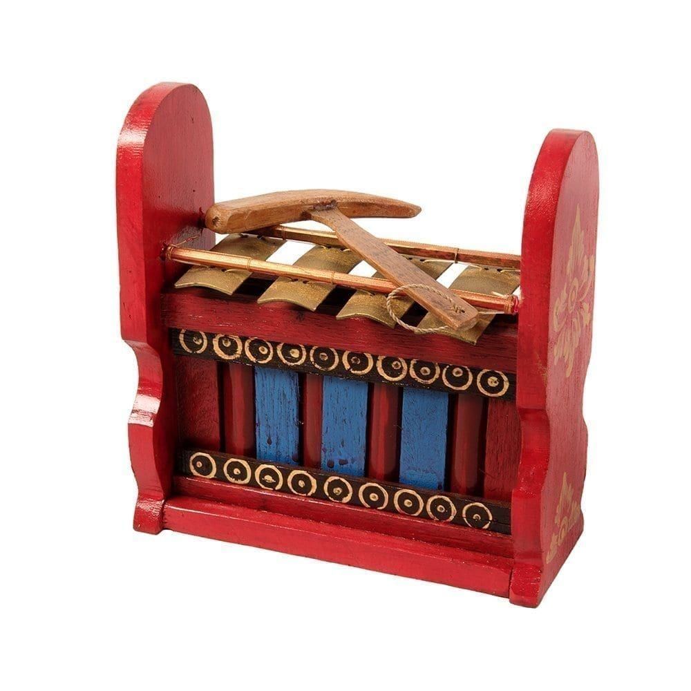 This is a product image of the Gamelan - Budget - Small 4 key. The instrument has four gold keys suspended by bamboo and wire. The casing is mainly red with some blue, gold and black decoration. A beater is laying on top of the instrument. The image has been taken from the front and the instrument is facing slightly to the left.