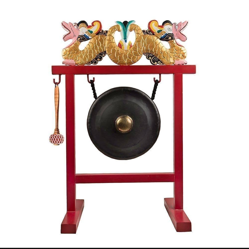This is a product image of the Gong Set - 12in (30cm) diameter Gong with Stand and Beater. The frame is a sleek metal design, painted red with a two ornate wooden dragons in red white and gold, sitting on the crossbar. The Gong is matt black with a gold boss and is hanging evenly from two hooks. The beater is attached to a hook on the left hand side of the stand. The entire stand is facing slightly to the left.