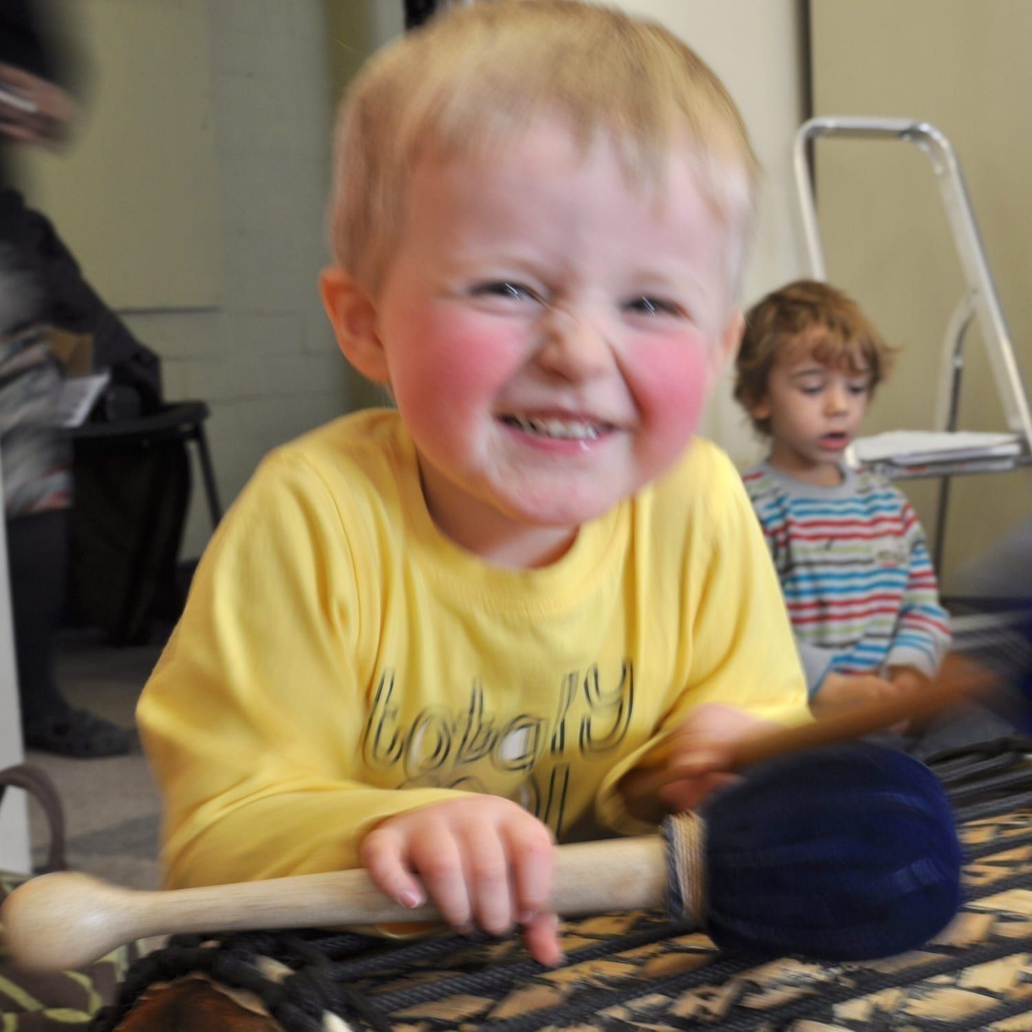 This is an action shot of an Early Years child smiling holding Drums for Schools' Dundun Bamboo beater