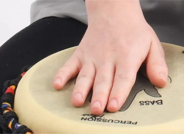 Close-up of a hand playing the bass area on a pre-tuned Djembe drum, showcasing proper technique for West African drumming.