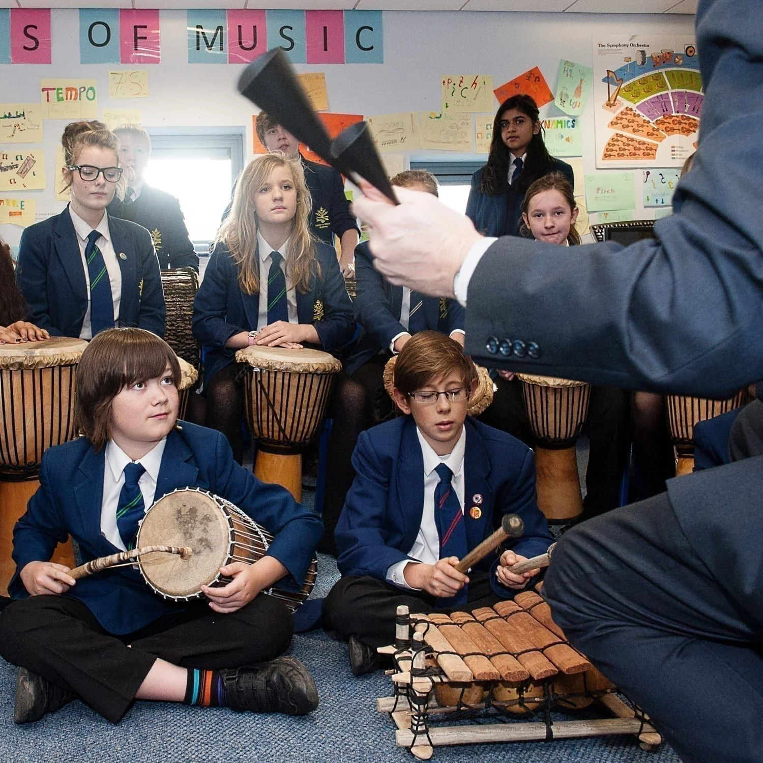 This is an action shot of some Secondary Schools children playing in a music workshop. They have a selection of West African instruments including a Talking Drum, a Balafon and Djembes. The teacher is partially in shot at the front with an Agogo.