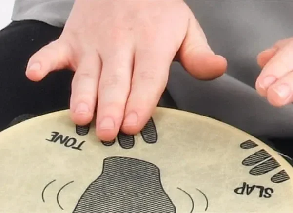 Close-up of hands playing a pre-tuned Djembe drum, highlighting labeled areas for tone and slap, ideal for learning West African drumming techniques.