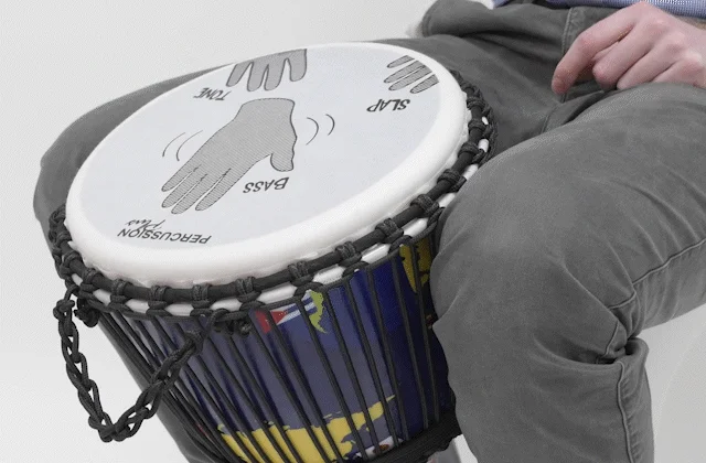 Hands playing a Slap Djembe drum with labeled hand positions for bass, tone, and slap, demonstrating correct drumming techniques.